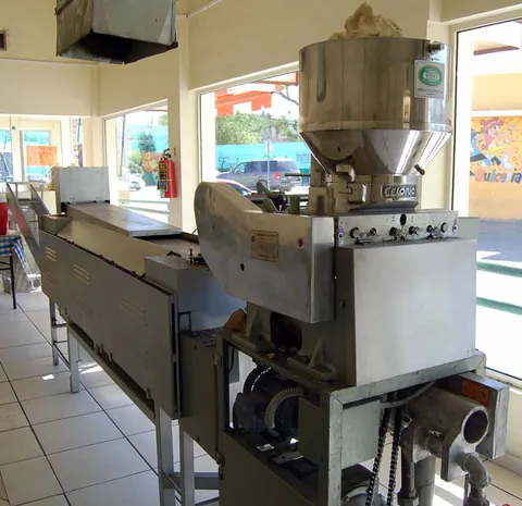 Interior de la tortillería con la máquina de tortillas en operación